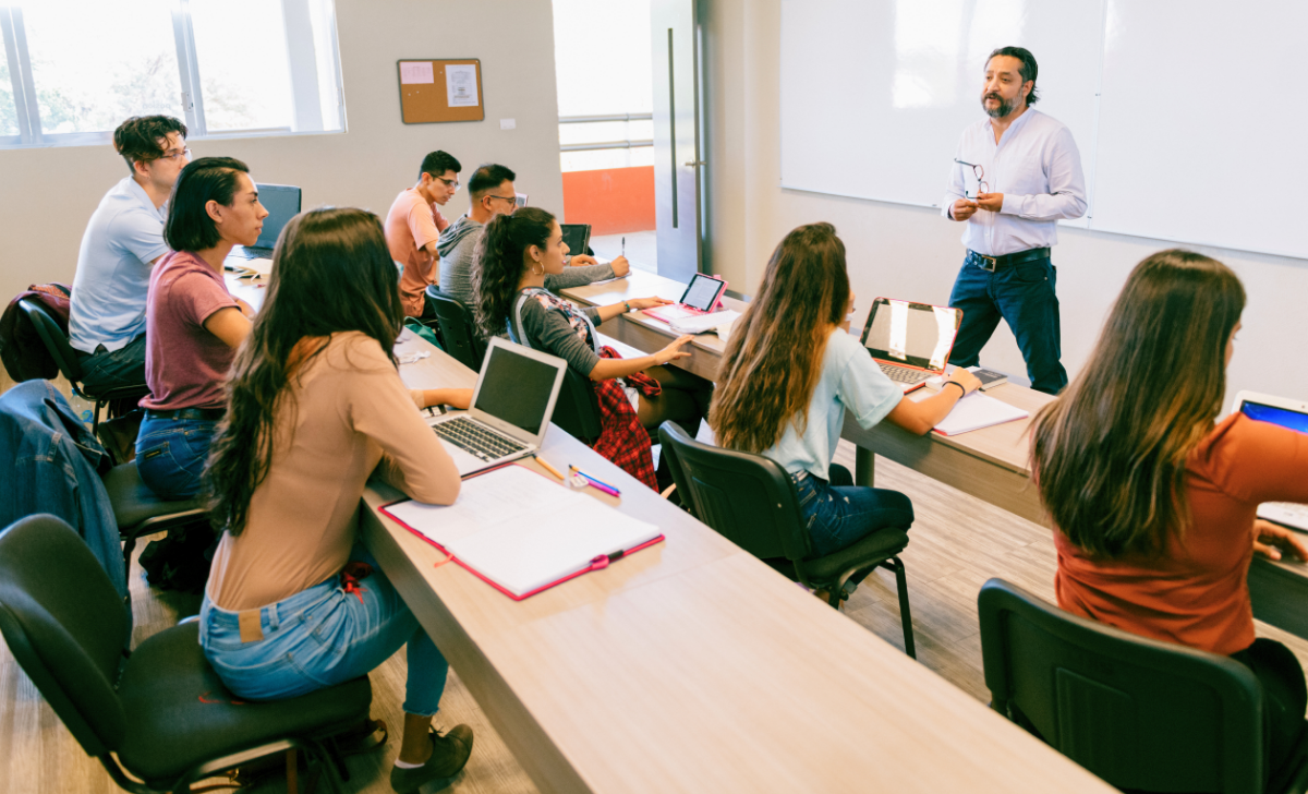 Persona estudiando ciberseguridad frente a una laptop, con libros de informática y un monitor que muestra un escudo de seguridad.